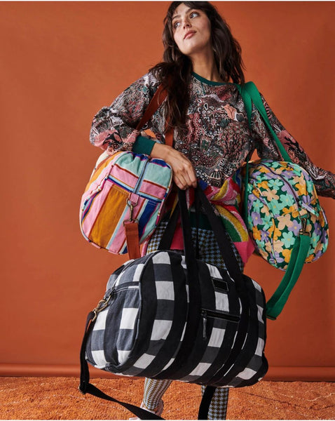 Model is wearing Kip & Co Bush Daisy Duffle Bag on her left shoulder, and carrying 2 other duffle bags of different designs on her right shoulder and right hand.