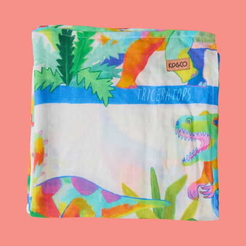 Kip & Co Dino Safari Bamboo Baby Swaddle folded and showing off the multicoloured dinos. In the top right corner  is a Kip & Co label.