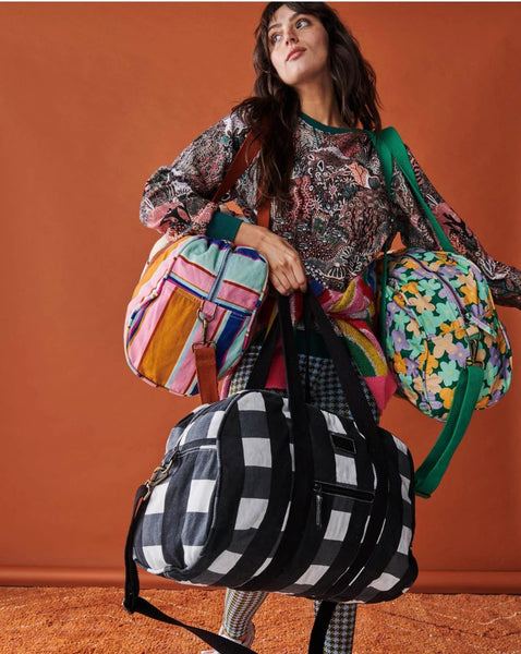Model is wearing Kip & Co Jaipur Stripe Duffle Bag on her right shoulder, and carrying 2 other duffle bags of different designs on her left shoulder and right hand.