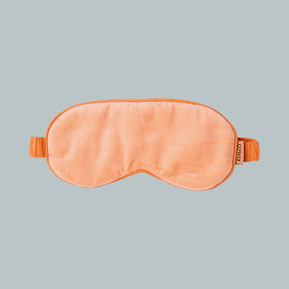 A peach-coloured sleep mask with a matching elastic strap, shown flat against a solid light gray background. The brand name 'Kip&Co' is visible on a small fabric tag on the right side of the mask.