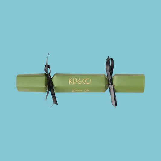 Packaging for Kip & Co Moss Velvet Eye Mask - Green Christmas cracker with black ribbons on a light blue background, featuring the brand 'Kip & Co'.