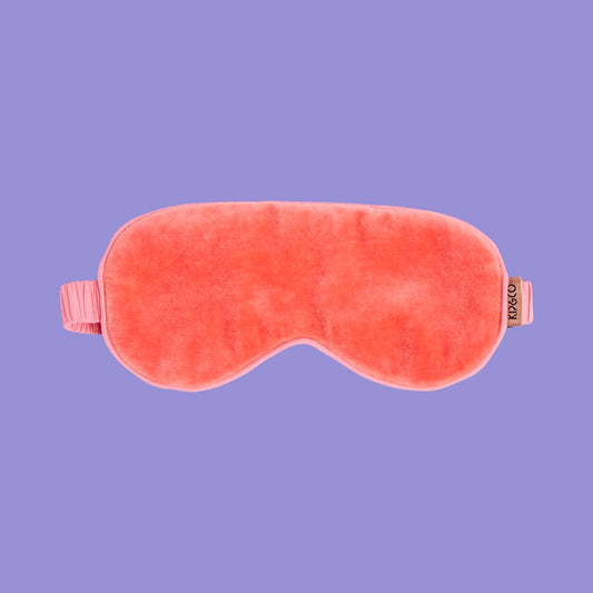 Coral-pink velvet eye mask on a purple background