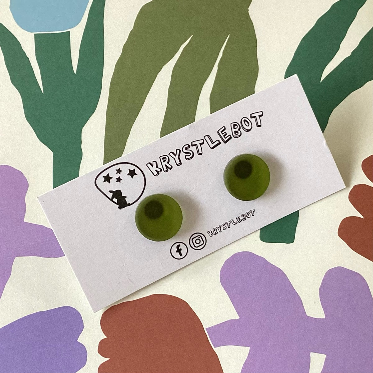 Olive green earrings on a Krystlebot branded card with colourful abstract shapes in the background