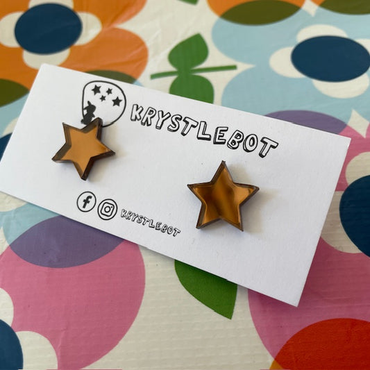 Krystlebot Star Studs - Bronze Mirror. Star-shaped earrings on a branded card with a colorful floral background