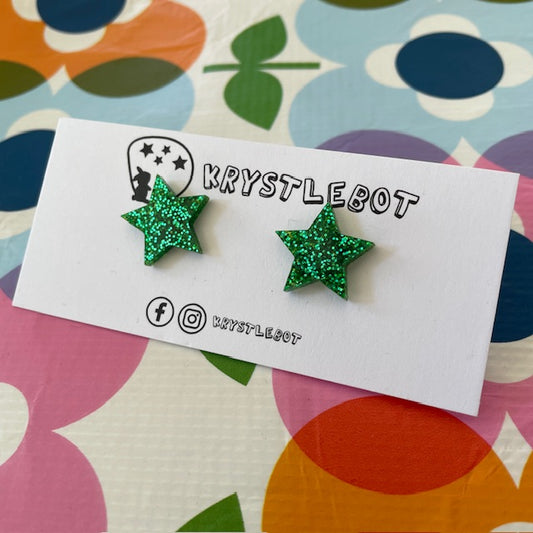 Krystlebot Star Studs - Green Glitter. Green star-shaped earrings on a Krystlebot branded card with a colorful floral background.