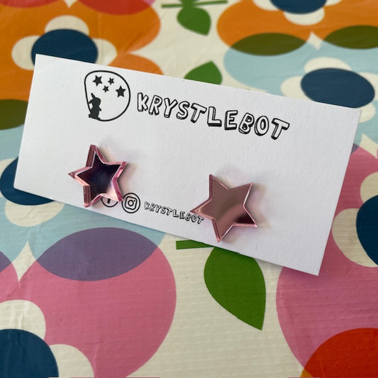 Krystlebot Star Studs - Light Pink Mirror. Star-shaped earrings on a 'KRYSTLEBOT' branded card with a colorful background