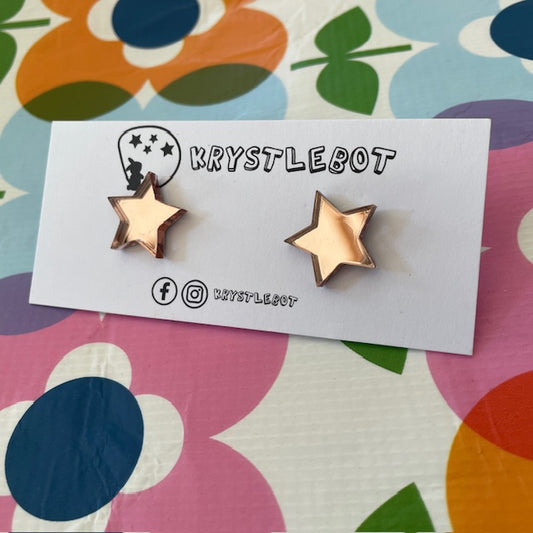 Krystlebot Star Studs - Peach Mirror. A pair of star-shaped earrings in a light pinky-brown mirror finish on a branded backing card.