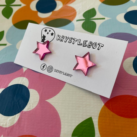 Krystlebot Star Studs - Pink Mirror. Pink star-shaped earrings on a 'KRYSTLEBOT' branded card with a colorful floral background.