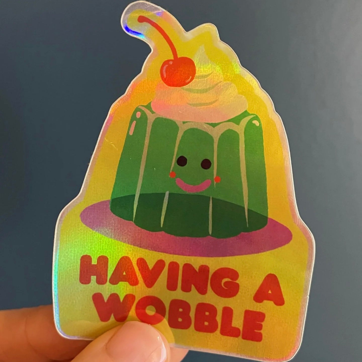 Holographic sticker by Naomi Wilkinson of a jelly with a cherry on top and 'Having a Wobble' text.