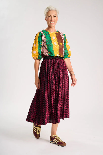 Model wearing a colourful top and maroon skirt on a white background