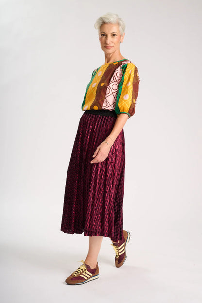 Side view of model wearing a colourful top and maroon skirt on a white background