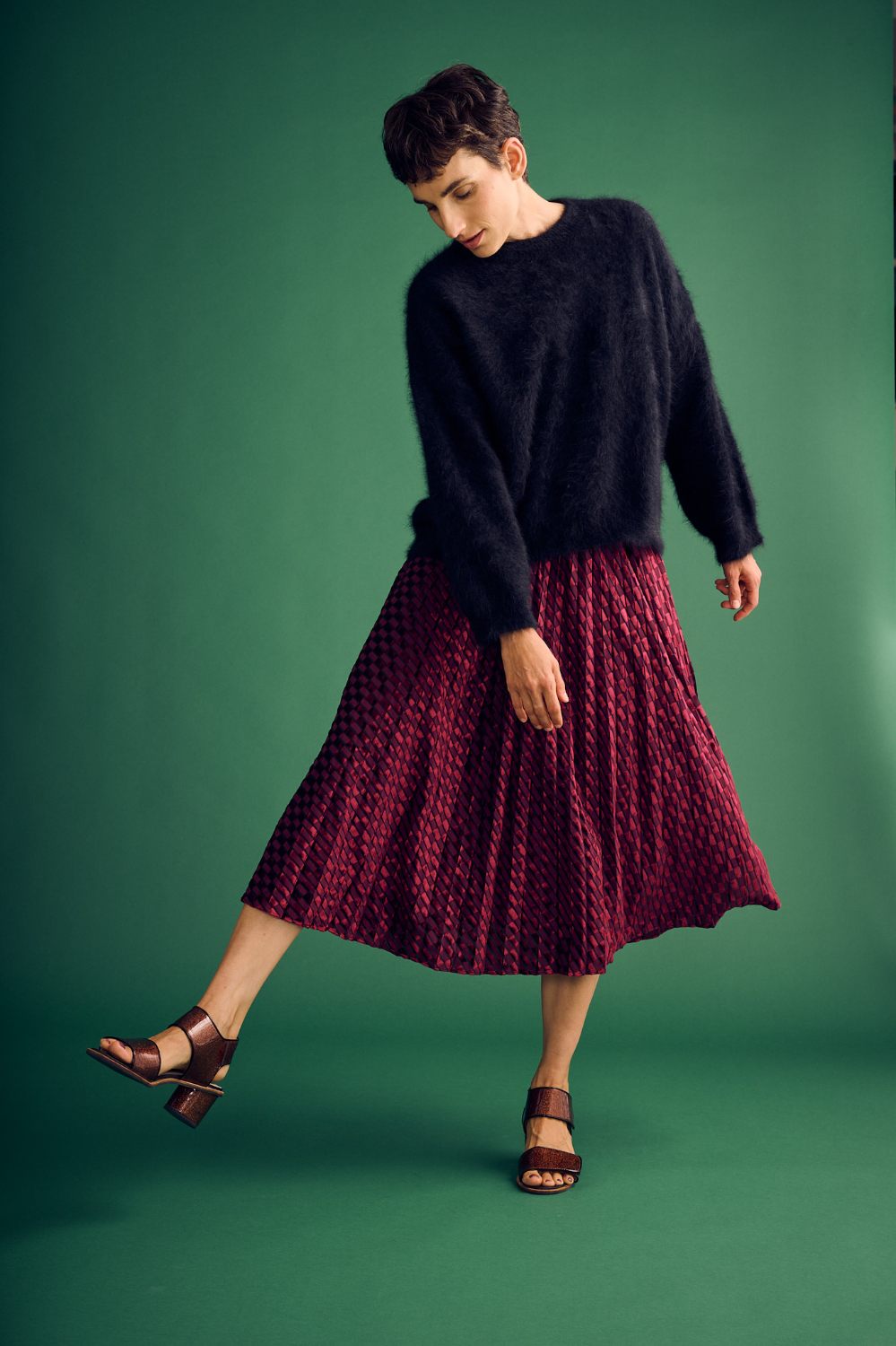 Woman wearing a black sweater and red skirt on a green background