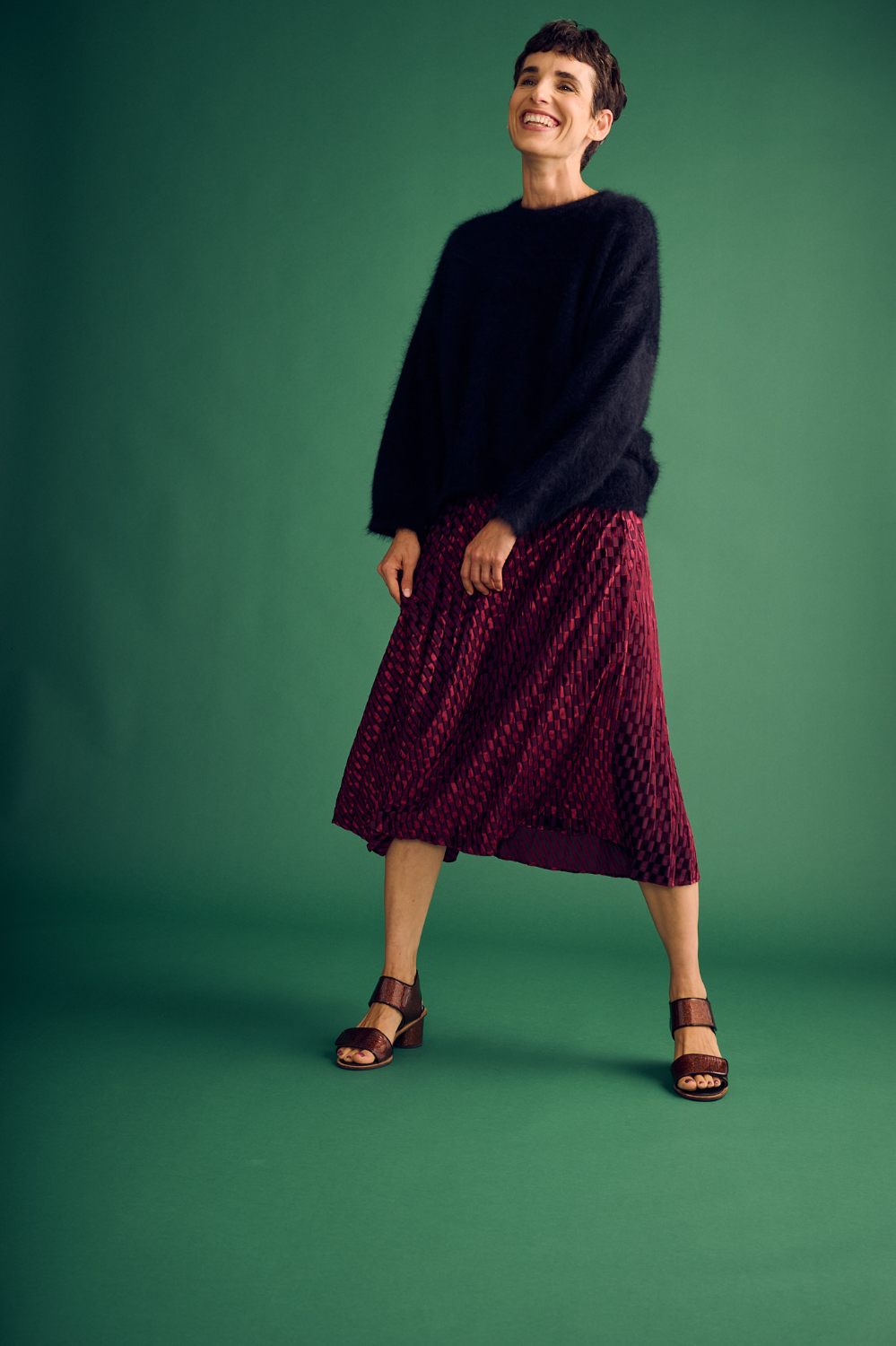 Woman wearing a black sweater and red patterned skirt on a green background