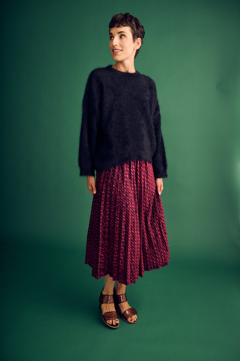 Woman wearing a black sweater and red patterned skirt against a green background