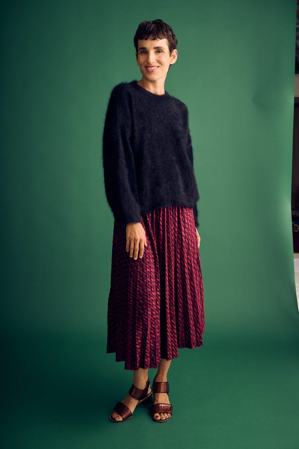 Woman wearing a dark sweater and red pleated skirt against a green background