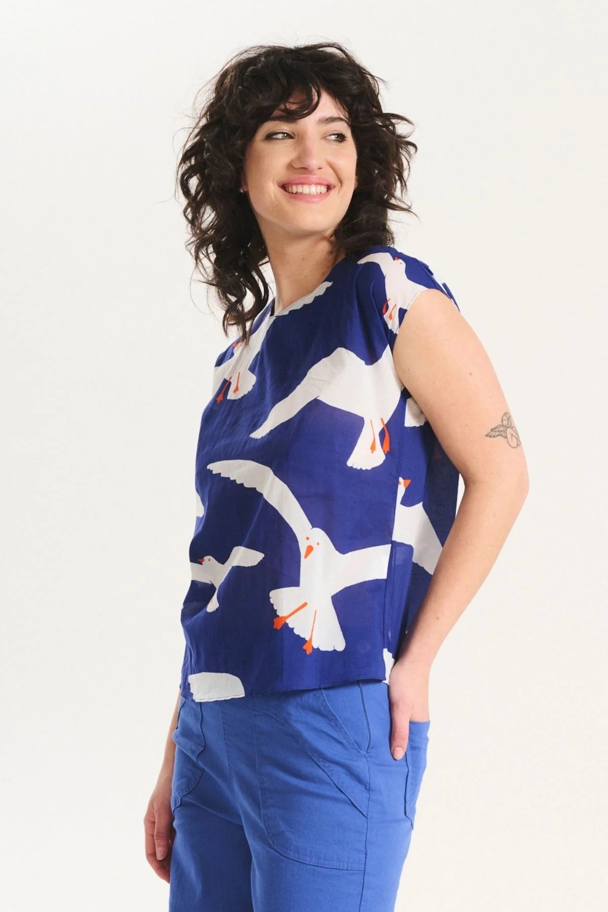 Woman wearing a blue sleeveless top with white bird pattern on a white background
