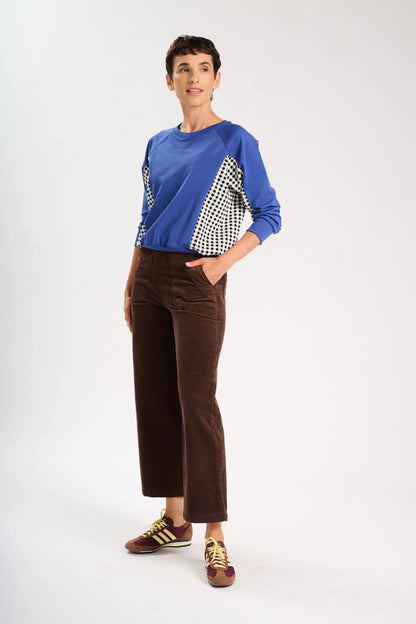 Side view of model standing and wearing a blue jumper and a pair of brown corduroy pants