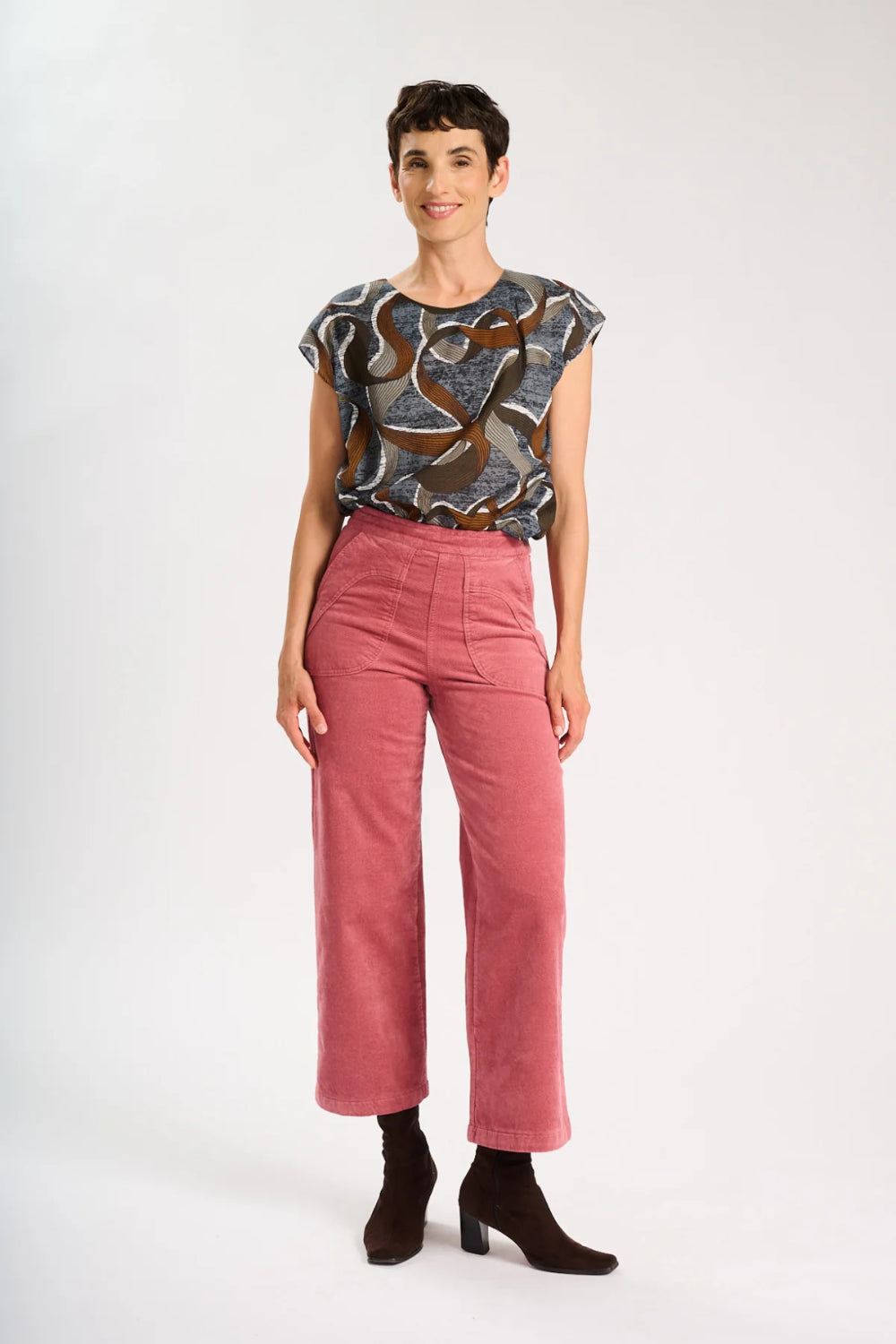 Model is standing with hands on her side, and wearing a a brown patterned top and pink corduroy pants