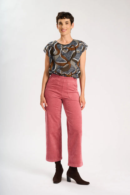 Model is standing with hands on her side, and wearing a a brown patterned top and pink corduroy pants
