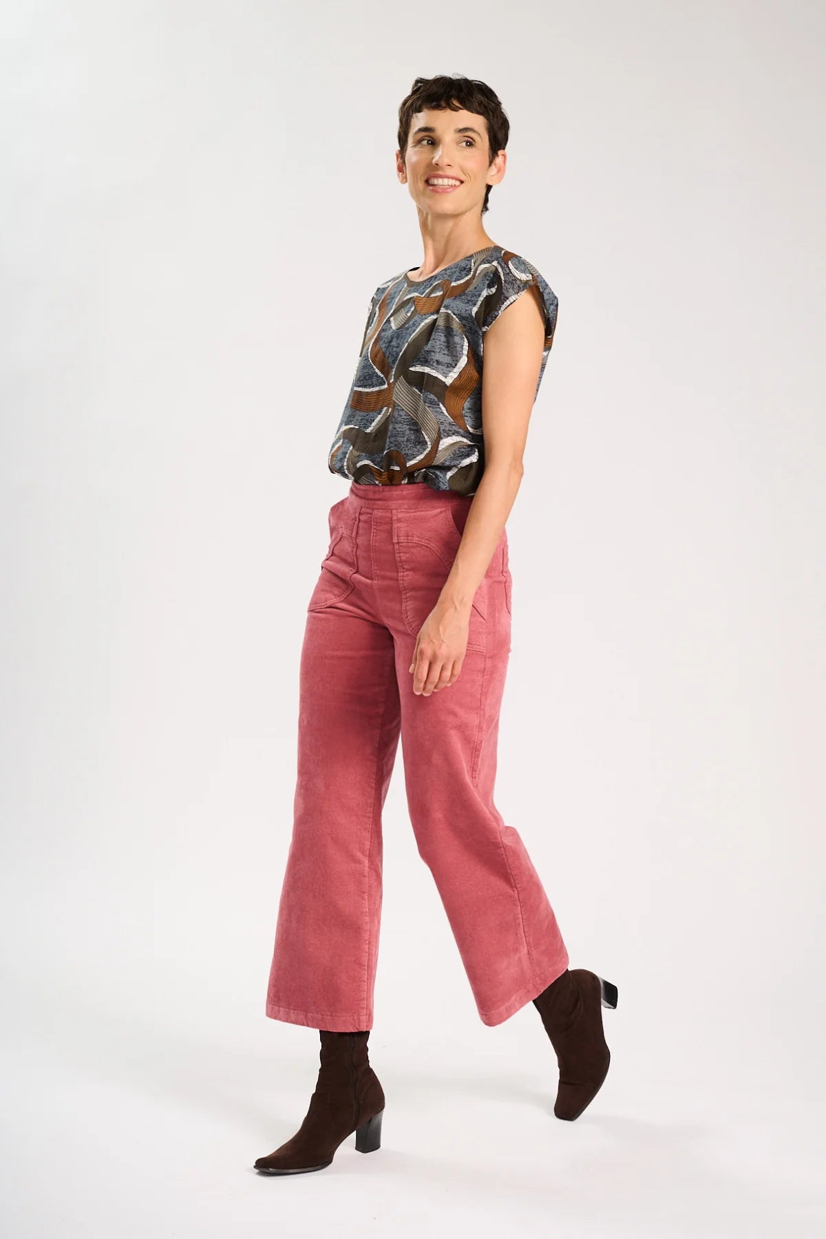 Side view of model wearing a brown patterned top and pink corduroy pants on a white background