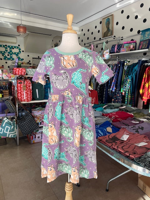 Front view of Mabel our shop mannequin wearing a cat patterned dress in a store setting with shelves and products in the background.