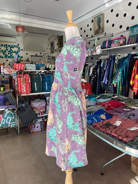 Side view of Mabel our shop mannequin wearing a cat patterned dress in a store setting with shelves and products in the background.