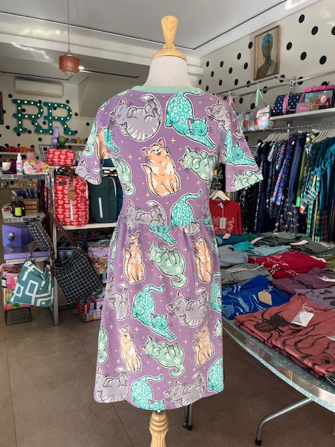 Back view of Mabel our shop mannequin wearing a cat patterned dress in a store setting with shelves and products in the background.