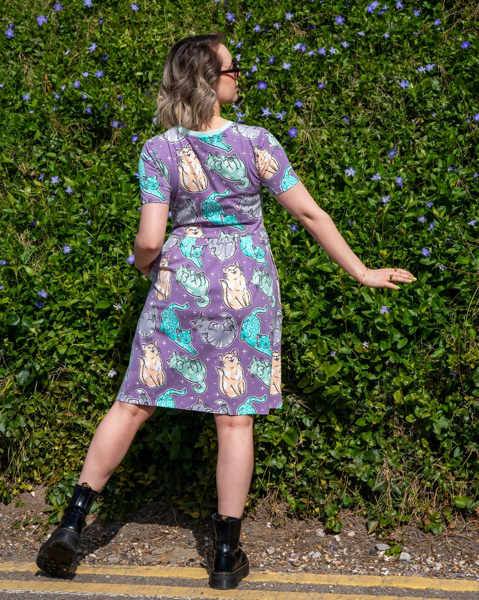 Back view of Person wearing a cat patterned dress standing in front of a green hedge.