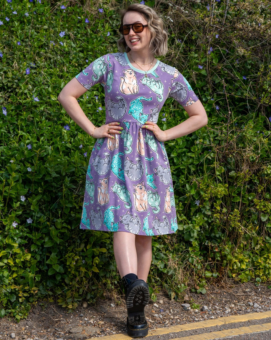 Woman wearing a car patterned dress standing outdoors with greenery in the background