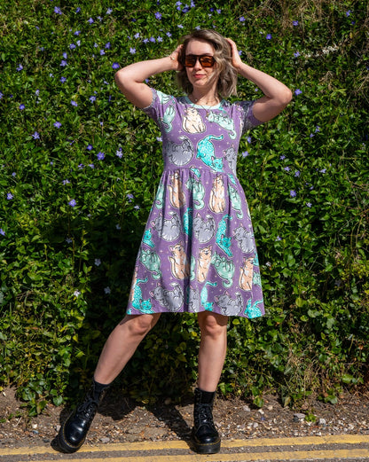 Woman wearing a cat patterned dress standing against a green hedge.
