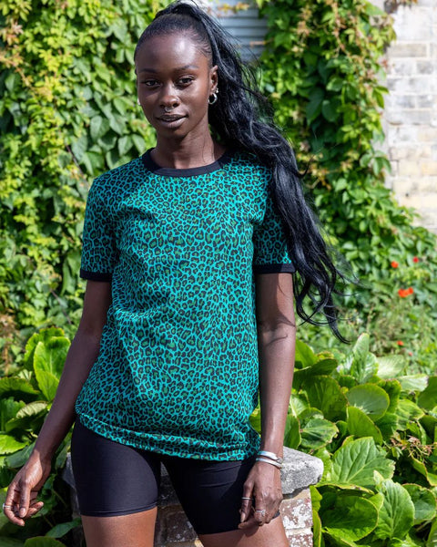Model is wearing Run and Fly Leopard Tee Shirt in Teal and paired with black shorts. She is facing the camera and smiling.