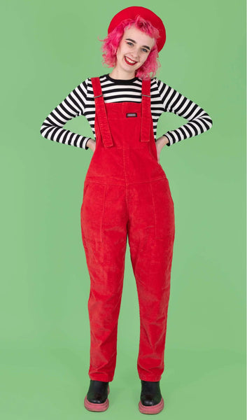 Model is wearing Run & Fly Red Cord Dungarees with a black and white striped long sleeve top underneath. Model's hands are on her hips.