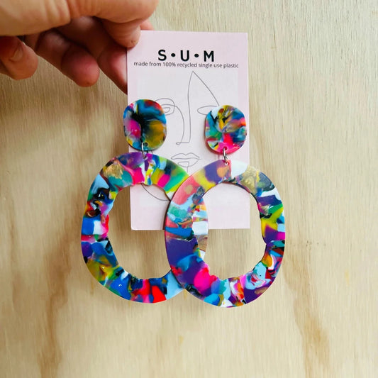 Colorful hoop earrings on a 'S.U.M' branded card against a wooden background