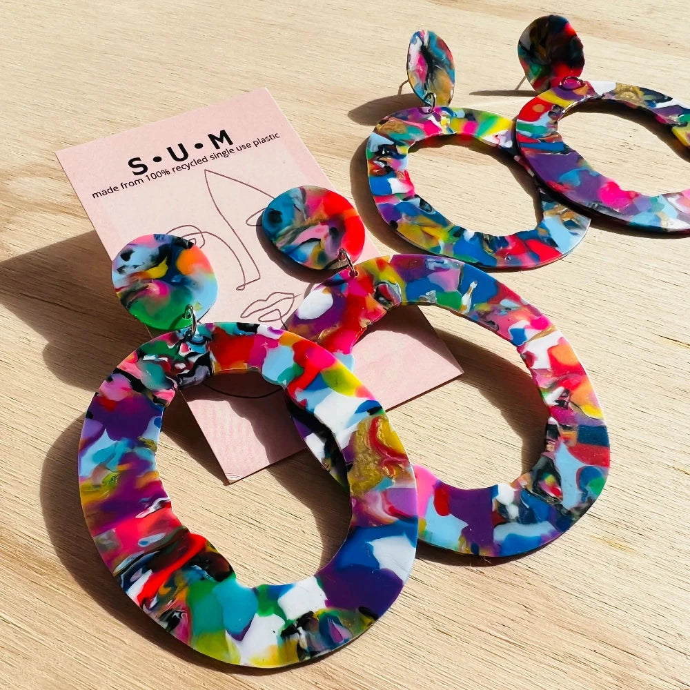 Colorful hoop earrings on a wooden surface with a 'S.U.M' card.